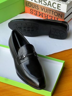 Black Clarks leather loafers with metal chain-bit hardware displayed in green Clarks box with luxury brand books.
