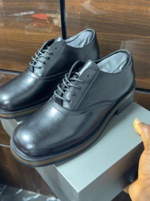 Cream leather formal lace-up shoes with black laces and layered sole displayed on a grey box.