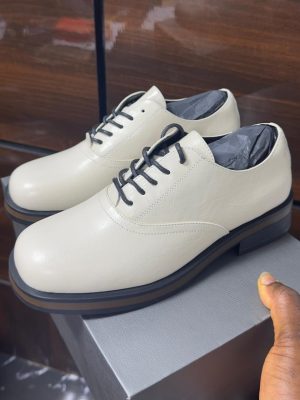 Cream leather formal lace-up shoes with black laces and layered sole displayed on a grey box.