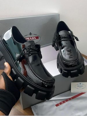 Black Prada patent leather chunky loafers with lug sole and rope laces displayed with grey Prada box and authenticity card.
