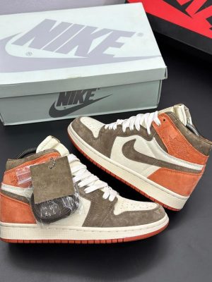 Brown and orange Nike Air Jordan 1 High sneakers with cream base and extra laces displayed with Nike box.
