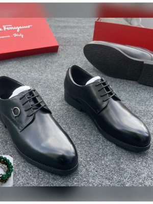Salvatore Ferragamo men’s cognac brown leather oxford shoes with brogue detailing and Gancini hardware, displayed beside red branded box on grey carpet background.