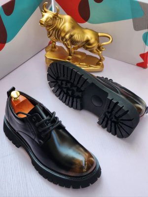 Men's luxury black leather derby boots with burnished brown toe cap, thick black lug sole, and contrast stitching, displayed next to a gold bull statue and colorful shoebox.