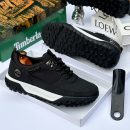 Men's luxury brown Timberland suede and black textile sneakers with white midsole and rugged black lug outsole sitting in an open shoebox.
