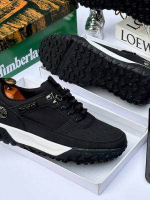 Men's luxury brown Timberland suede and black textile sneakers with white midsole and rugged black lug outsole sitting in an open shoebox.
