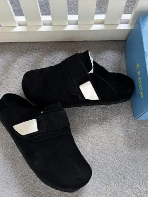 Men's luxury beige suede slip-on mules with velcro strap closure and cushioned sole on grey carpet next to blue shoebox.