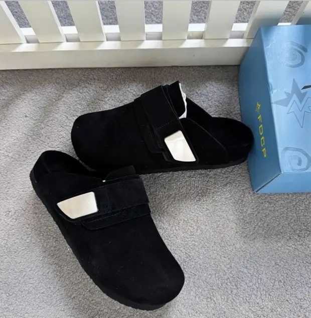 Premium beige suede slip-on mules Men's luxury beige suede slip-on mules with velcro strap closure and cushioned sole on grey carpet next to blue shoebox.