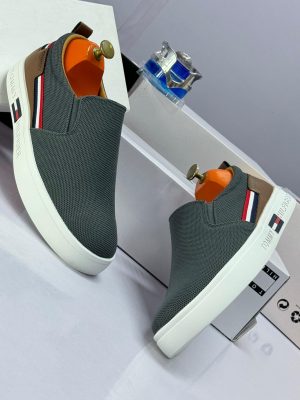 Alt Text: Black knit Tommy Hilfiger slip-on sneakers with white platform sole and red, white, blue flag stripe - luxury men's casual shoes.
