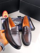 Dark brown leather penny loafers held in hand with tan lining, displayed with black shoe box and shoe polish.