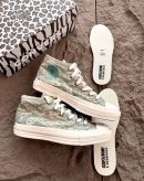 Converse x Undefeated Chuck 70 high-top sneakers in black canvas with off-white rubber sole and heel branding, held in hand with patterned shoebox and insoles visible on textured background.