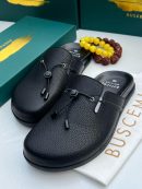 Buscemi men's leather slide mules in cream and black with pebbled texture, bungee cord detail, and green branded boxes displayed on dark slatted surface.