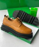 Bottega Veneta men's tan pebbled leather chunky derby shoes with thick black lug sole, displayed in signature green shoebox with branded tin.