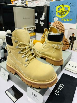 Men's luxury wheat suede combat boots with black leather collar, silver hardware, and chunky gum lug soles displayed on shoeboxes.