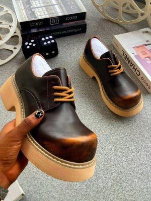 Men's luxury brown burnished leather platform oxford shoes with tan laces and cream sole resting on a grey shoebox.