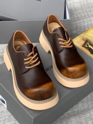 Men's luxury brown burnished leather platform oxford shoes with tan laces and cream sole resting on a grey shoebox.