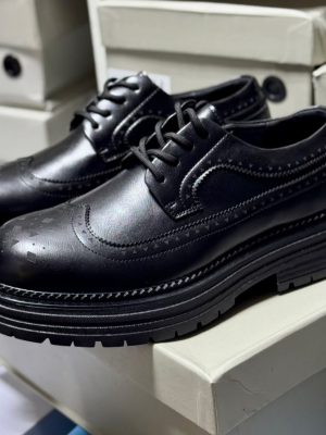 Men's luxury cognac brown leather brogue oxford shoes with geometric toe cap detailing and thick black ridged sole sitting on white shoeboxes.