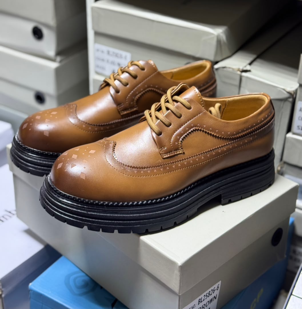 Premium cognac leather brogues Men's luxury cognac brown leather brogue oxford shoes with geometric toe cap detailing and thick black ridged sole sitting on white shoeboxes.