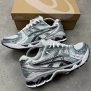 ASICS GEL-Kayano 14 men's sneakers in silver, white, and blue with visible GEL cushioning units, displayed on grey concrete surface with open cardboard shoebox.
