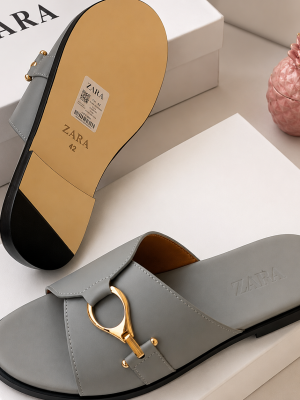 Zara men's slide sandals in black and grey with gold horsebit buckle hardware, displayed with white Zara shoebox and dust bag on dark slatted surface.