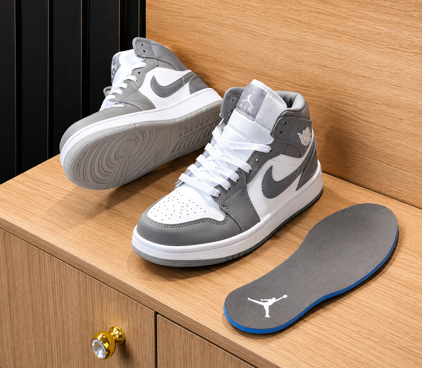 Air Jordan 1 High sneakers in white and medium grey leather with white laces and grey outsole, displayed on wooden surface alongside grey Jordan branded insole.