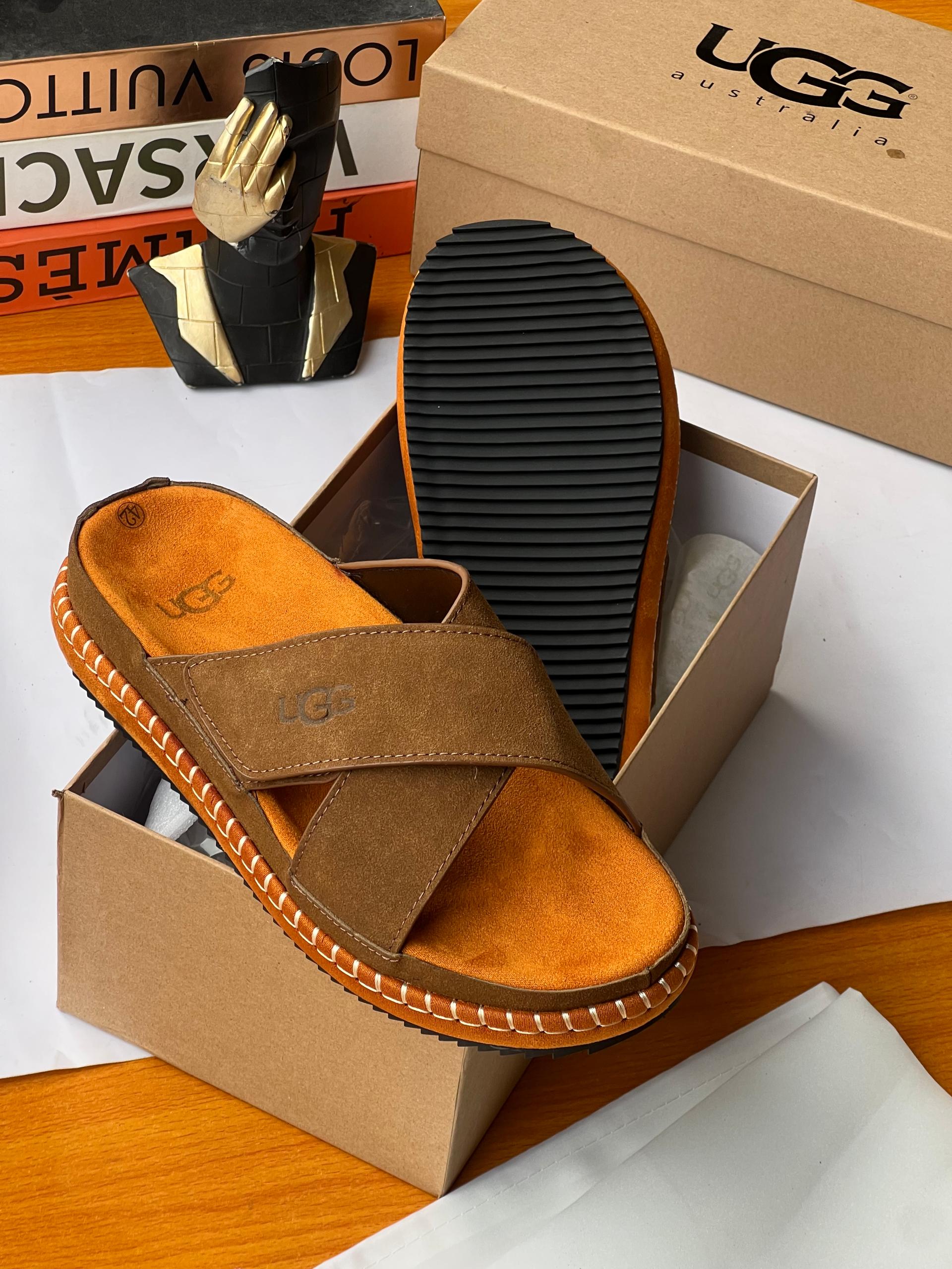 Authentic UGG suede cross-strap slides Black UGG suede cross-strap slides with white contrast stitching and chunky sole displayed with UGG box and dust bag.