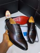 Dark brown John Foster leather Oxford dress shoes with cap toe and red leather sole displayed in box with shoe polish.