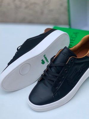 Black Lacoste leather sneakers with white sole and tan heel tab displayed with green Lacoste box.