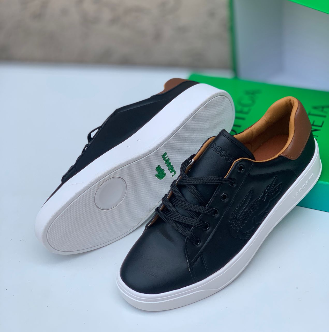 Premium Lacoste leather sneakers Black Lacoste leather sneakers with white sole and tan heel tab displayed with green Lacoste box.
