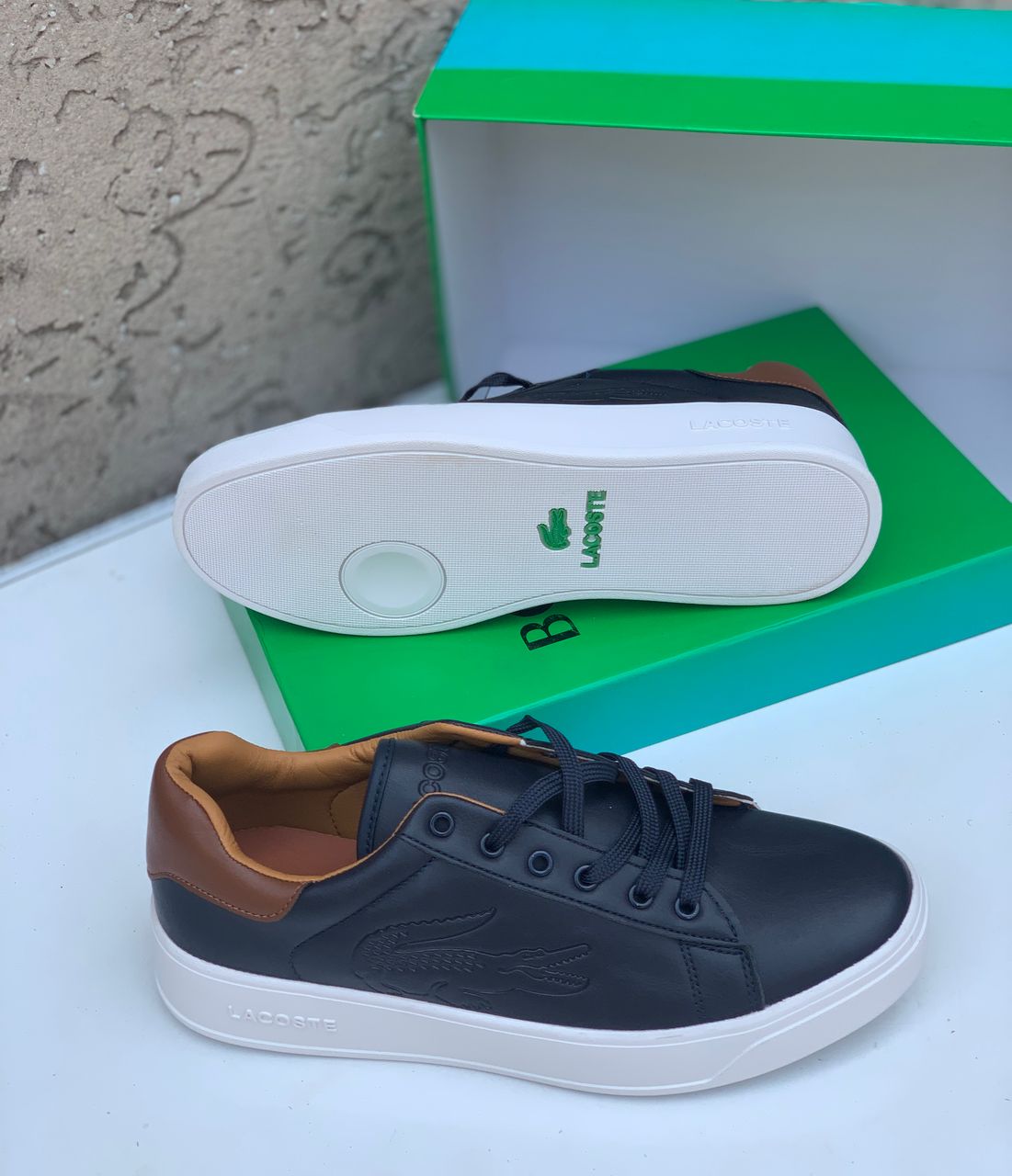 Premium Lacoste leather sneakers Black Lacoste leather sneakers with white sole and tan heel tab displayed with green Lacoste box.