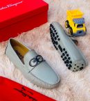 Green Salvatore Ferragamo pebbled leather driving loafers with silver Gancini hardware and rubber pebble sole displayed on fluffy rug with red Ferragamo box.