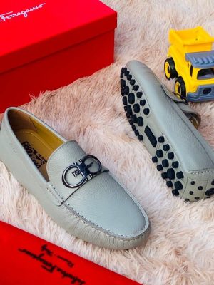 Green Salvatore Ferragamo pebbled leather driving loafers with silver Gancini hardware and rubber pebble sole displayed on fluffy rug with red Ferragamo box.