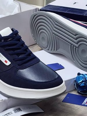 Navy blue Tommy Hilfiger leather sneakers with white sole and red stripe detail displayed with Tommy box and blue skull decor.