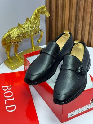 Black pebbled leather loafers with metal buckle hardware displayed on red box with golden horse statue.
