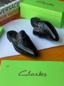 Black Clarks leather mule loafers with geometric textured vamp and metal bit displayed with green Clarks boxes.