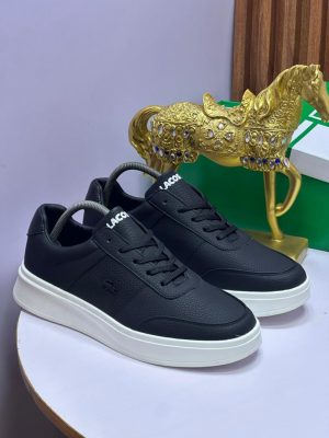 Black Lacoste pebbled leather sneakers with white sole displayed on white surface with gold horse statue and green box.