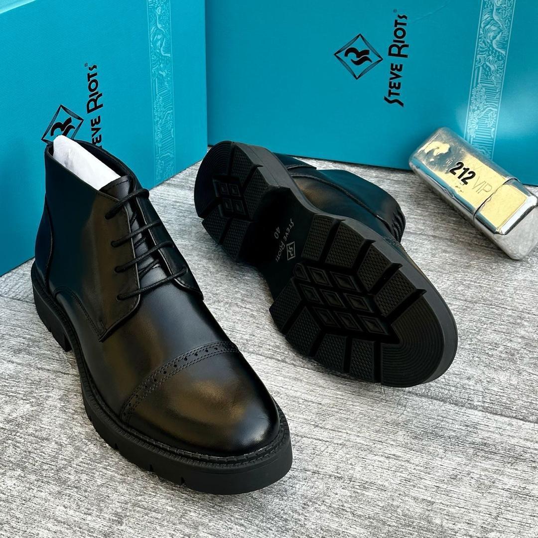 Steve Riots men’s black brogue boots Steve Riots men’s black leather cap-toe brogue boots with glossy finish, perforated detailing, and rugged lug sole, displayed beside turquoise branded box and metallic VIP tag on textured grey surface.