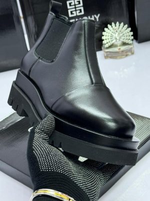 Givenchy men's black leather Chelsea boots with chunky platform sole, held by gloved hand against branded box background.