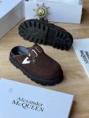 Alexander McQueen men’s brown suede slip-on sandals with silver triangular buckle and thick black lug sole, displayed with branded white box and dust bag on wooden surface.