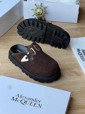 Alexander McQueen men’s brown suede slip-on sandals with silver triangular buckle and thick black lug sole, displayed with branded white box and dust bag on wooden surface.