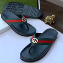 Gucci men's black rubber thong sandals with green and red Web stripe strap and gold interlocking G logo, displayed with branded box and gold elephant figurine.