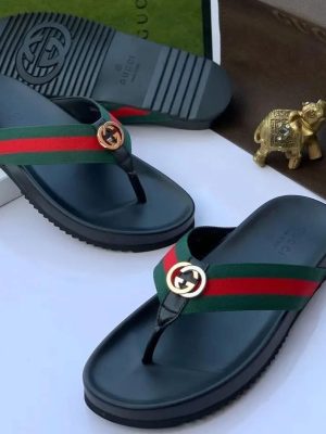 Gucci men's black rubber thong sandals with green and red Web stripe strap and gold interlocking G logo, displayed with branded box and gold elephant figurine.