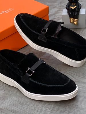 Santoni men's black suede loafer sneakers with tonal leather strap, silver hardware, and white rubber sole, displayed with orange branded shoebox on grey wood floor.