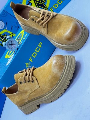 FDCP men's mustard distressed suede chunky boots with rope laces and thick ridged platform sole, displayed with blue branded shoebox and vintage alarm clock on white surface.