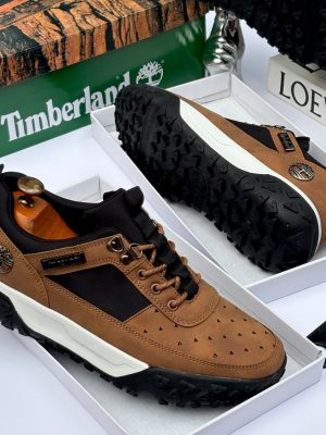 Men's luxury brown Timberland suede and black textile sneakers with white midsole and rugged black lug outsole sitting in an open shoebox.