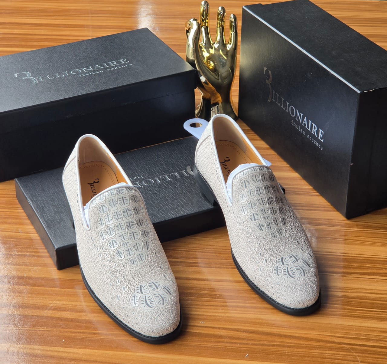 Pristine white Billionaire Italian Couture loafers Men's luxury white Billionaire Italian Couture loafers with embossed medallion pattern and blue soles resting on black branded shoeboxes.