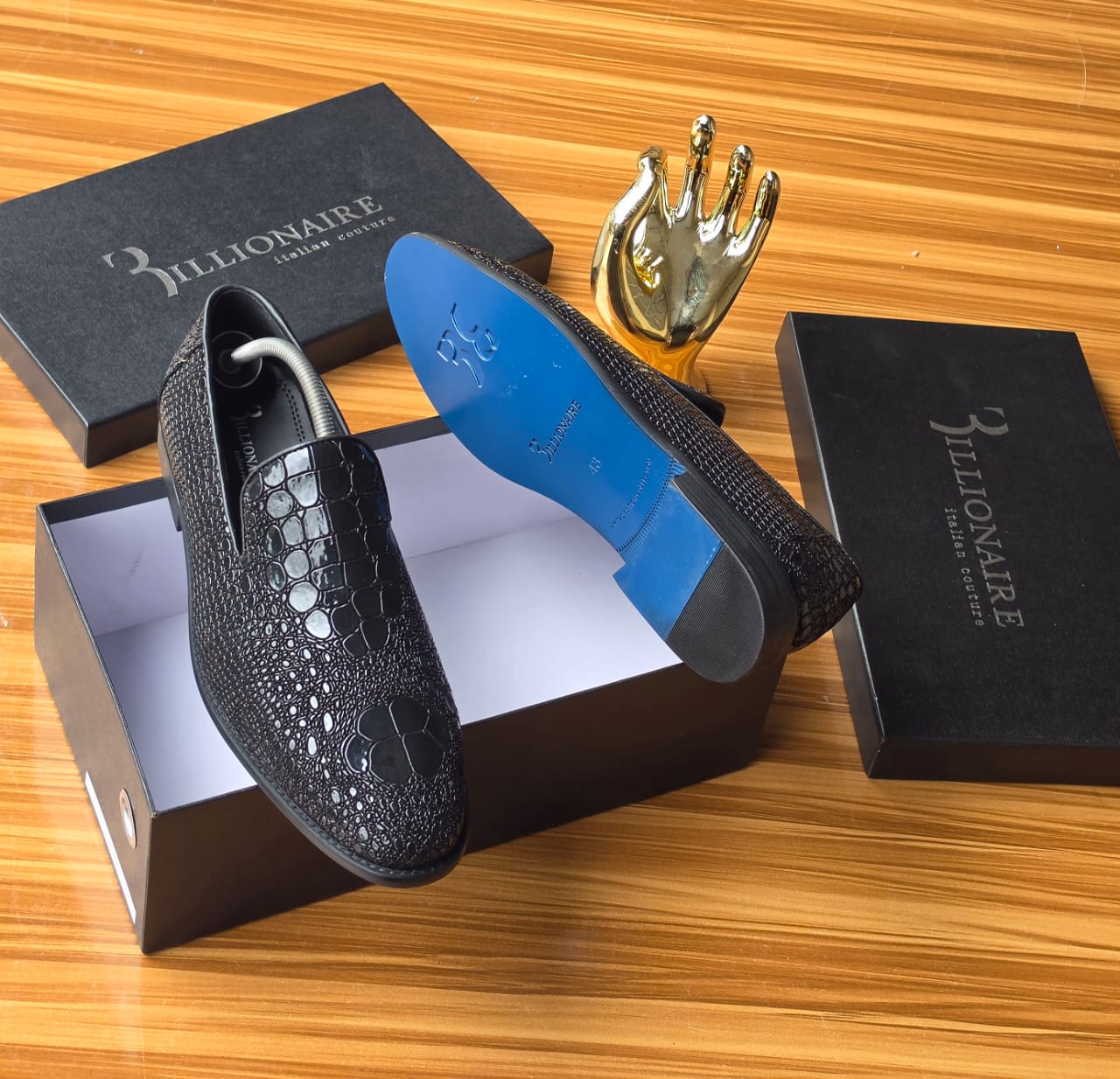 Dark Billionaire Italian Couture loafers Men's luxury dark brown Billionaire Italian Couture loafers with embossed medallion pattern and blue soles resting on black branded shoeboxes.