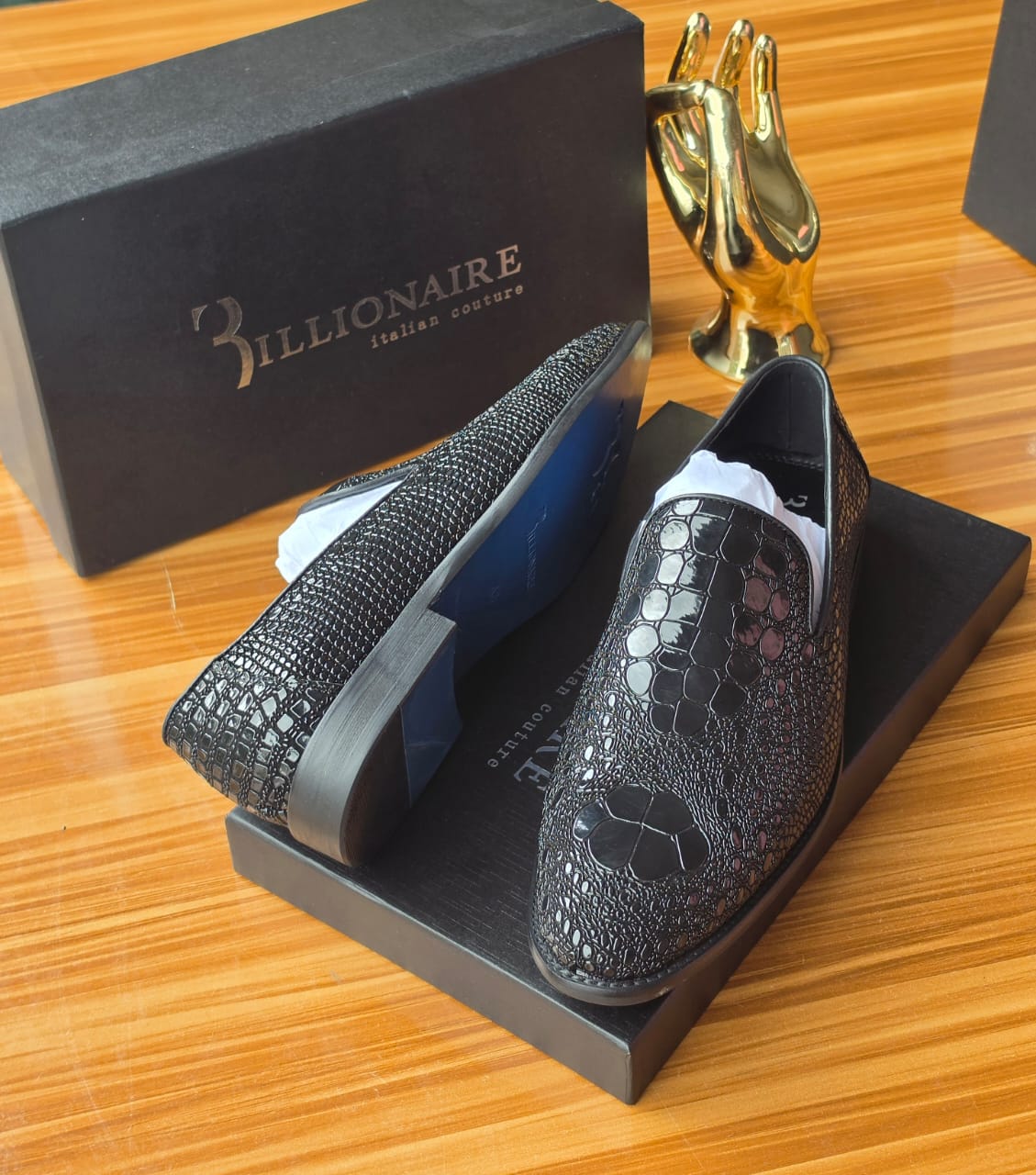 Dark Billionaire Italian Couture loafers Men's luxury dark brown Billionaire Italian Couture loafers with embossed medallion pattern and blue soles resting on black branded shoeboxes.
