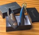 Men's luxury dark brown Billionaire Italian Couture loafers with embossed medallion pattern and blue soles resting on black branded shoeboxes.