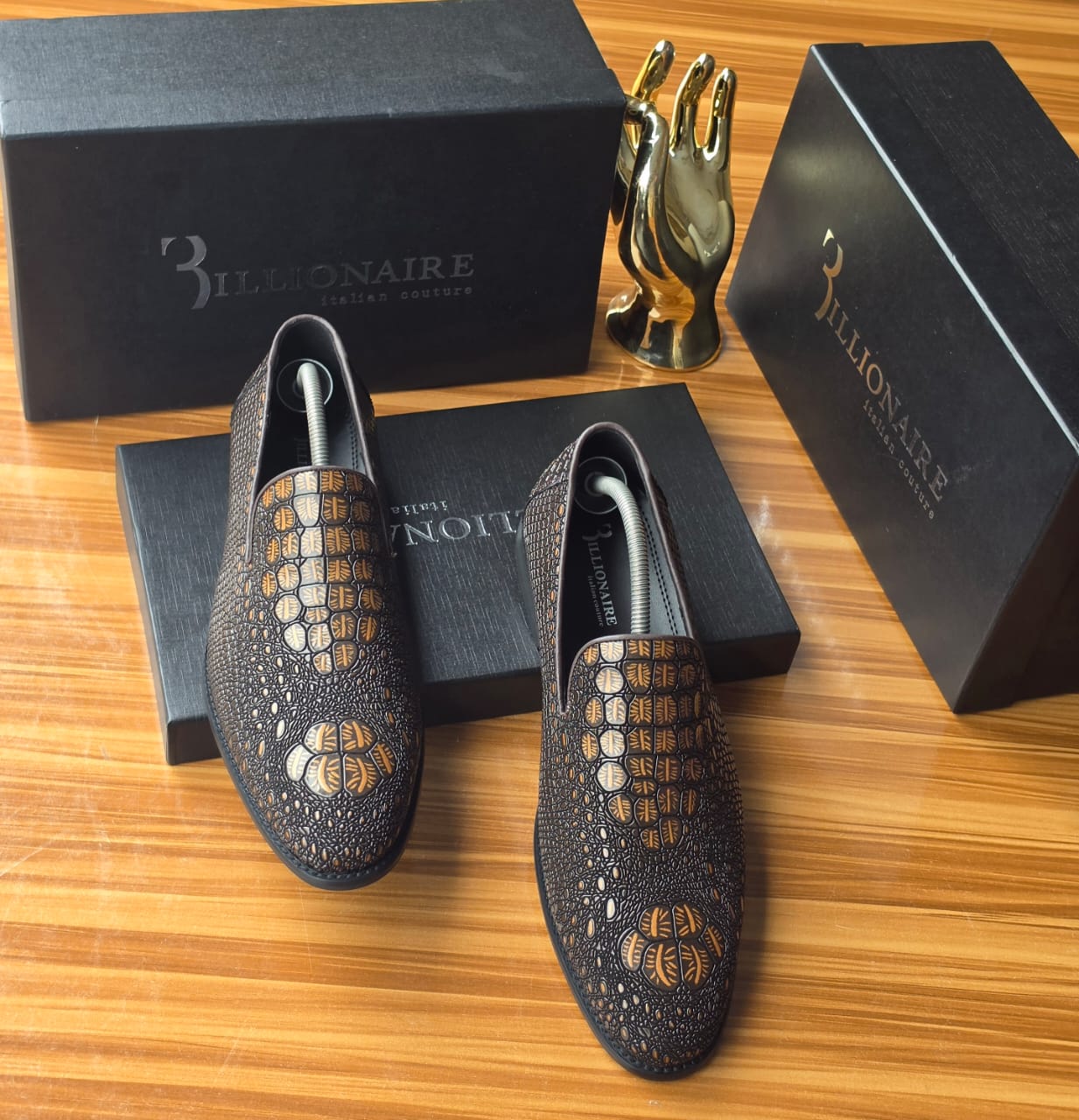 Dark Billionaire Italian Couture loafers Men's luxury dark brown Billionaire Italian Couture loafers with embossed medallion pattern and blue soles resting on black branded shoeboxes.