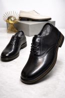 Men's luxury black leather oxford dress shoes with a thick sole and tan midsole accent resting on a marble surface.